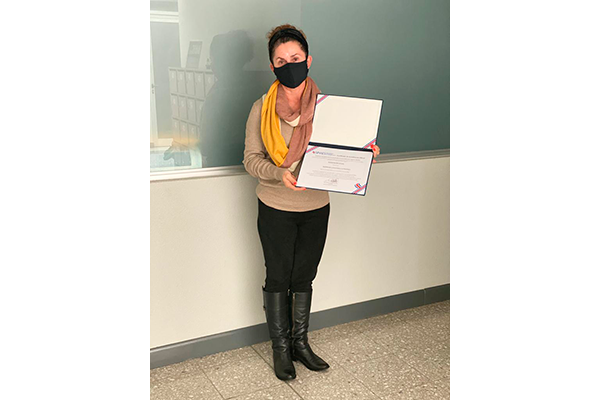 Docente Lynnethe Chaves Coordinadora de la Carrera de Psicología Sede Occidente sosteniendo el título de Acreditación
